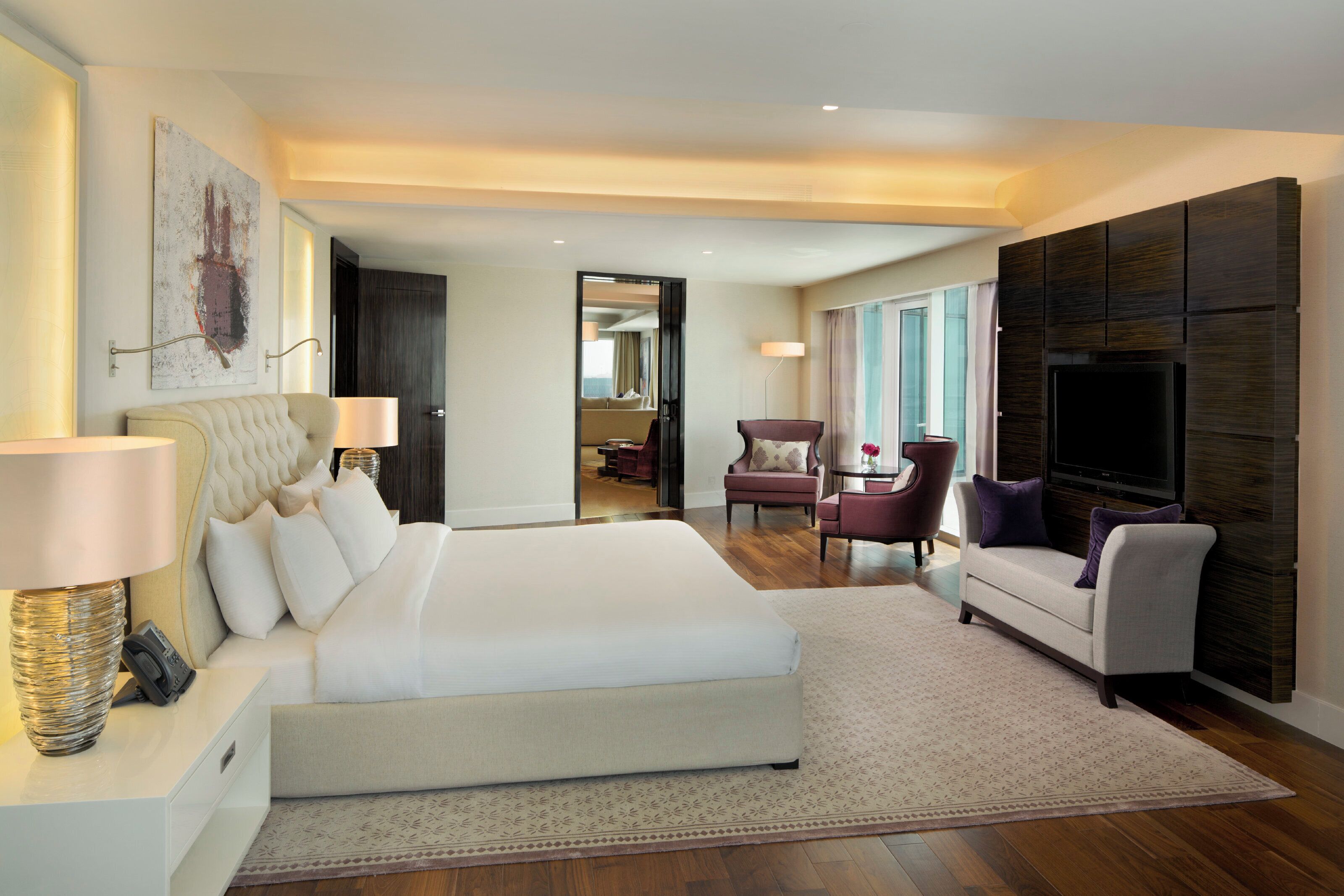 A modern hotel room with a large bed, a sofa, a TV, and a desk with a lamp.