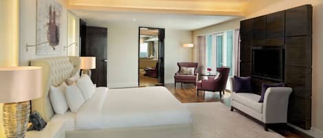 A modern hotel room with a large bed, a sofa, a TV, and a desk with a lamp.