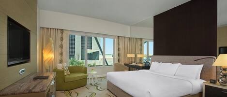 A modern hotel room with a large bed, a desk, a television, and a view of a building outside.