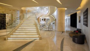 A modern hotel lobby with a central spiral staircase, glass railings, and a seating area with round tables.