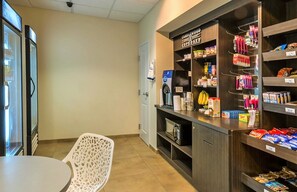A kitchenette area with a microwave, coffee maker, and a shelf stocked with snacks and beverages.
