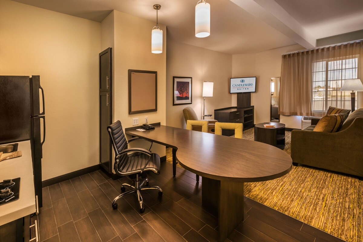 A hotel room with a dining table, chairs, a television, a sofa, and a refrigerator.