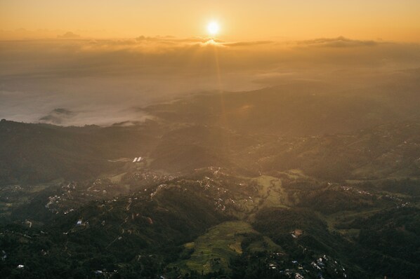 An aerial view of a valley with a sunrise or sunset, featuring a mix of forested areas and scattered buildings. - Dwarika's Sanctuary - A Himalayan Wellness Retreat (Dhulikhel)