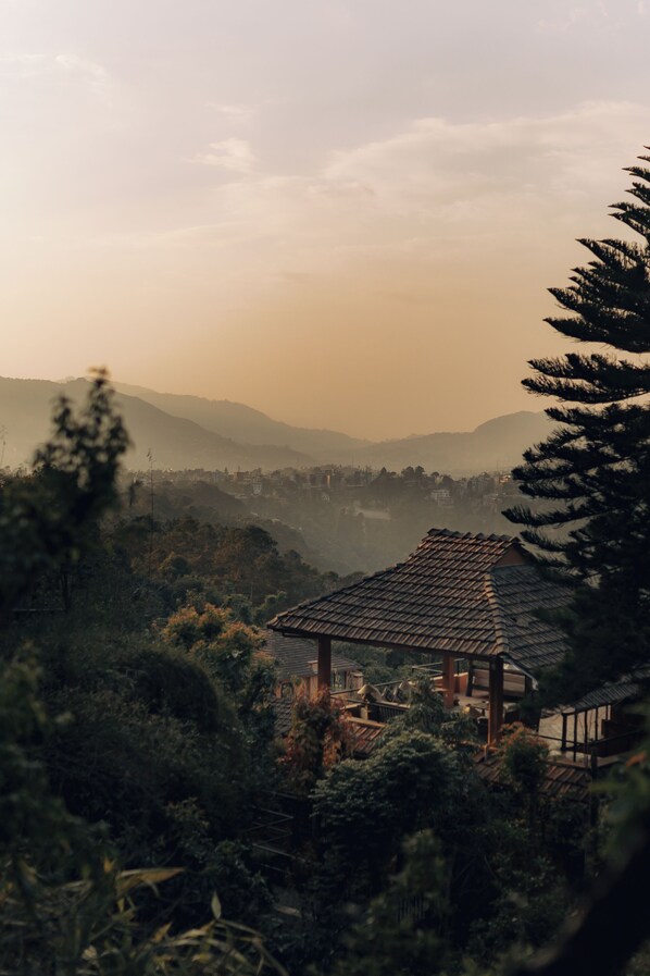 A traditional wooden structure surrounded by dense foliage and hills in the background. - Dwarika's Sanctuary - A Himalayan Wellness Retreat (Dhulikhel)