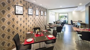 A modern dining area with tables and chairs, framed pictures on the wall, and a view of the outdoors. - The Lotus - Apartment Hotel, Venkatraman Street (Chennai)