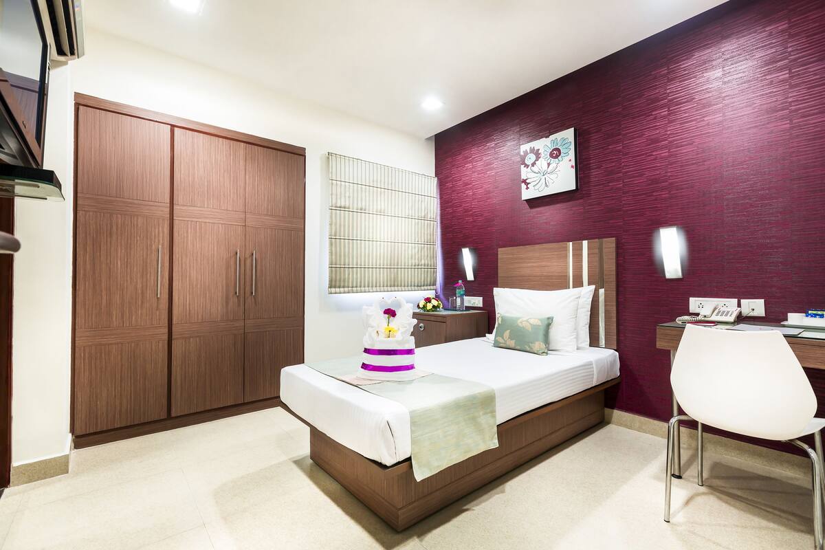 Ein Hotelzimmer mit Bett, Schreibtisch, Stuhl, Kleiderschrank und einem Fenster mit Jalousien.