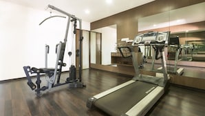 Une salle de sport moderne équipée d’un tapis de course, d’une machine de musculation et d’un mur recouvert de miroirs.