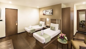 A hotel room with two beds, a small table with a vase of flowers, a mirror, and a wooden wardrobe. - The Lotus - Apartment Hotel, Venkatraman Street (Chennai)