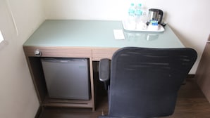Une chambre compacte comprenant un petit réfrigérateur, un bureau avec une chaise, ainsi qu’un plateau avec des bouteilles d’eau et une machine à café.