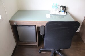 Een kleine kamer met een minibar, een bureau met stoel, en een dienblad met waterflesjes en een koffiezetapparaat.