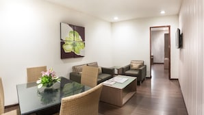 A modern hotel room with a glass dining table, wicker chairs, a sofa, a coffee table, and a painting on the wall. - The Lotus - Apartment Hotel, Venkatraman Street (Chennai)