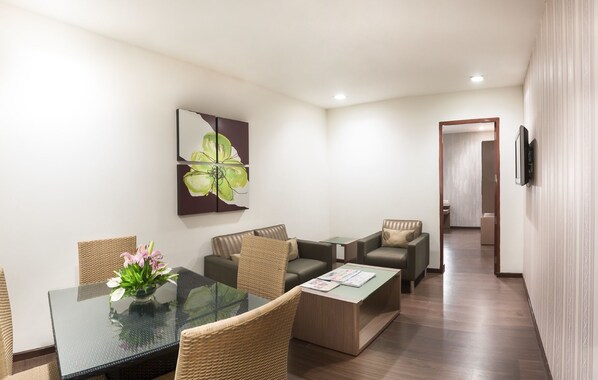 Een moderne hotelkamer met een glazen eettafel, rieten stoelen, een bank, een bijzettafeltje en een schilderij aan de muur.