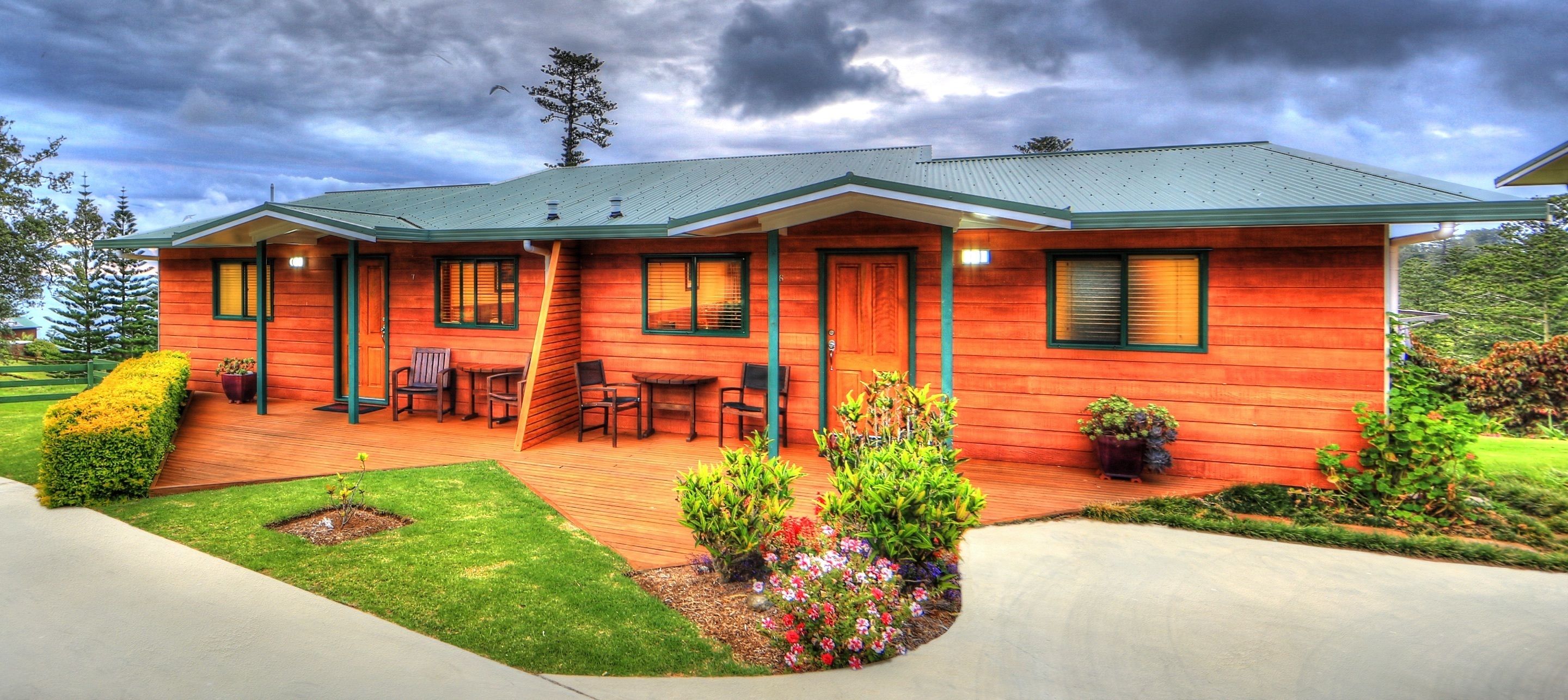 A two-story wooden cabin with a covered patio, outdoor seating, and a landscaped garden.