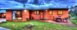 Une maison moderne à deux étages, avec une façade en bois, de grandes fenêtres et une terrasse aménagée avec du mobilier d’extérieur.