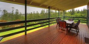 Une terrasse extérieure couverte, dotée d’une table et de chaises, qui offre une vue sur une zone boisée.