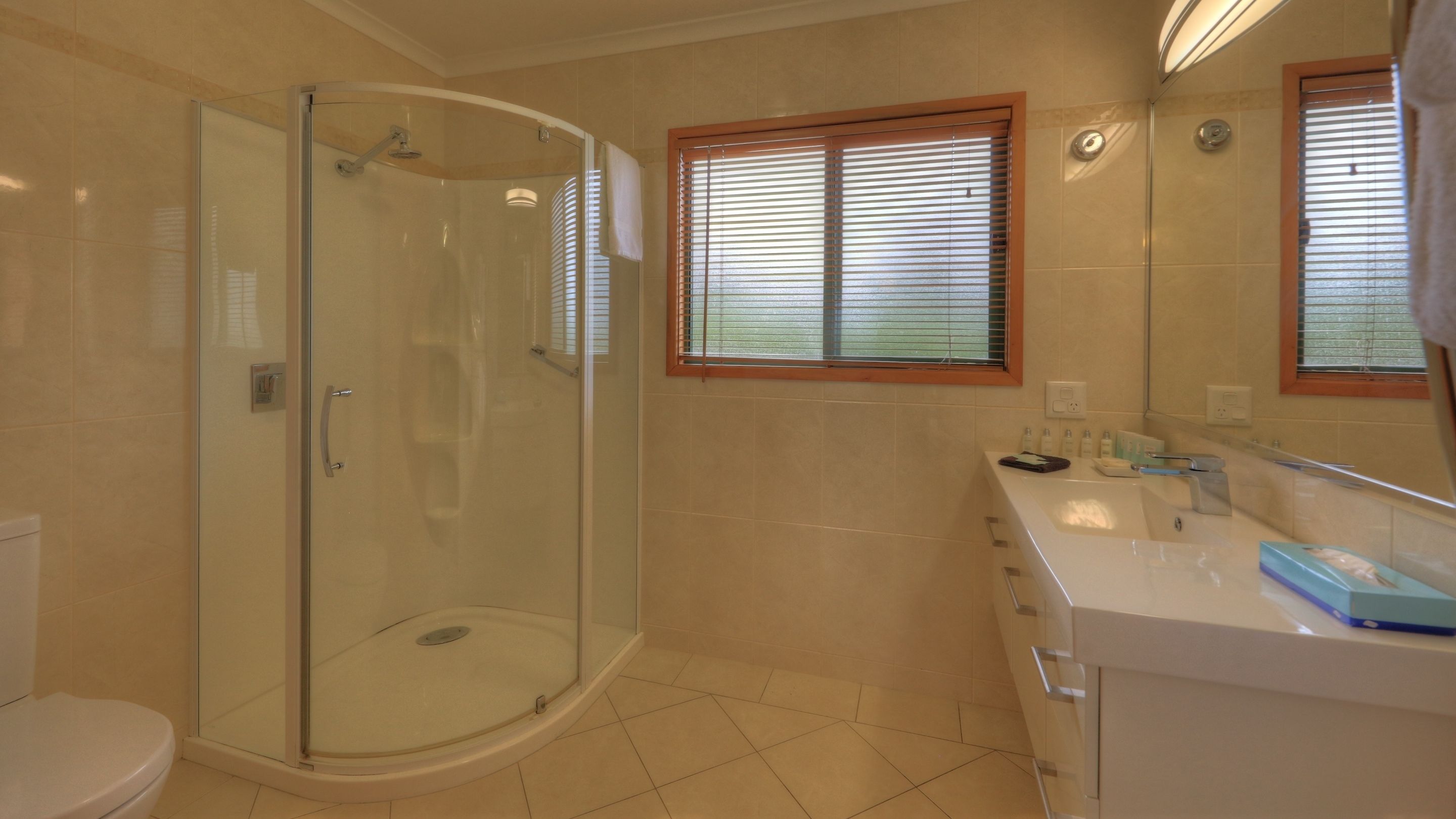 Un baño con ducha envuelta en vidrio, tocador con lavabo y ventana con persianas.