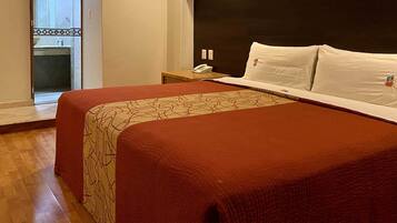 Quarto de hotel com uma cama grande, uma mesinha de cabeceira com telefone e vista para um banheiro com pia e espelho.