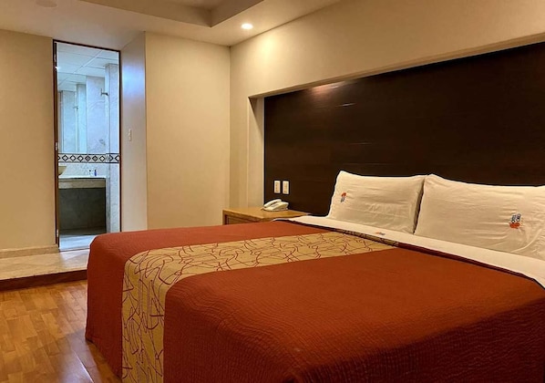 Une chambre d’hôtel avec deux lits, un plancher en bois, une tête de lit sombre et une petite table de chevet avec un téléphone.