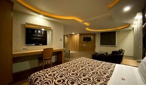Une chambre d’hôtel moderne dotée d’un plafond incurvé, d’un lit avec une couvre-lit à motifs, d’un bureau avec une chaise, d’un téléviseur à écran plat et d’une armoire.