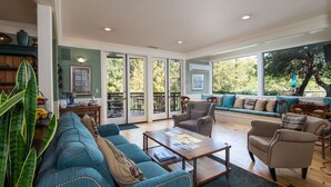 Un salon spacieux comprenant un canapé, des fauteuils, une table basse et une table à manger. Une porte-fenêtre coulissante donne accès à un espace extérieur avec une table et des chaises de patio.