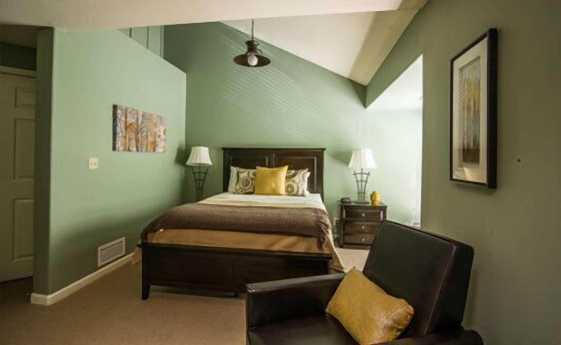 A bedroom with a bed, a chair, a nightstand, a lamp, and a painting on the wall.