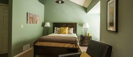 A bedroom with a bed, a chair, a nightstand, a lamp, and a painting on the wall.