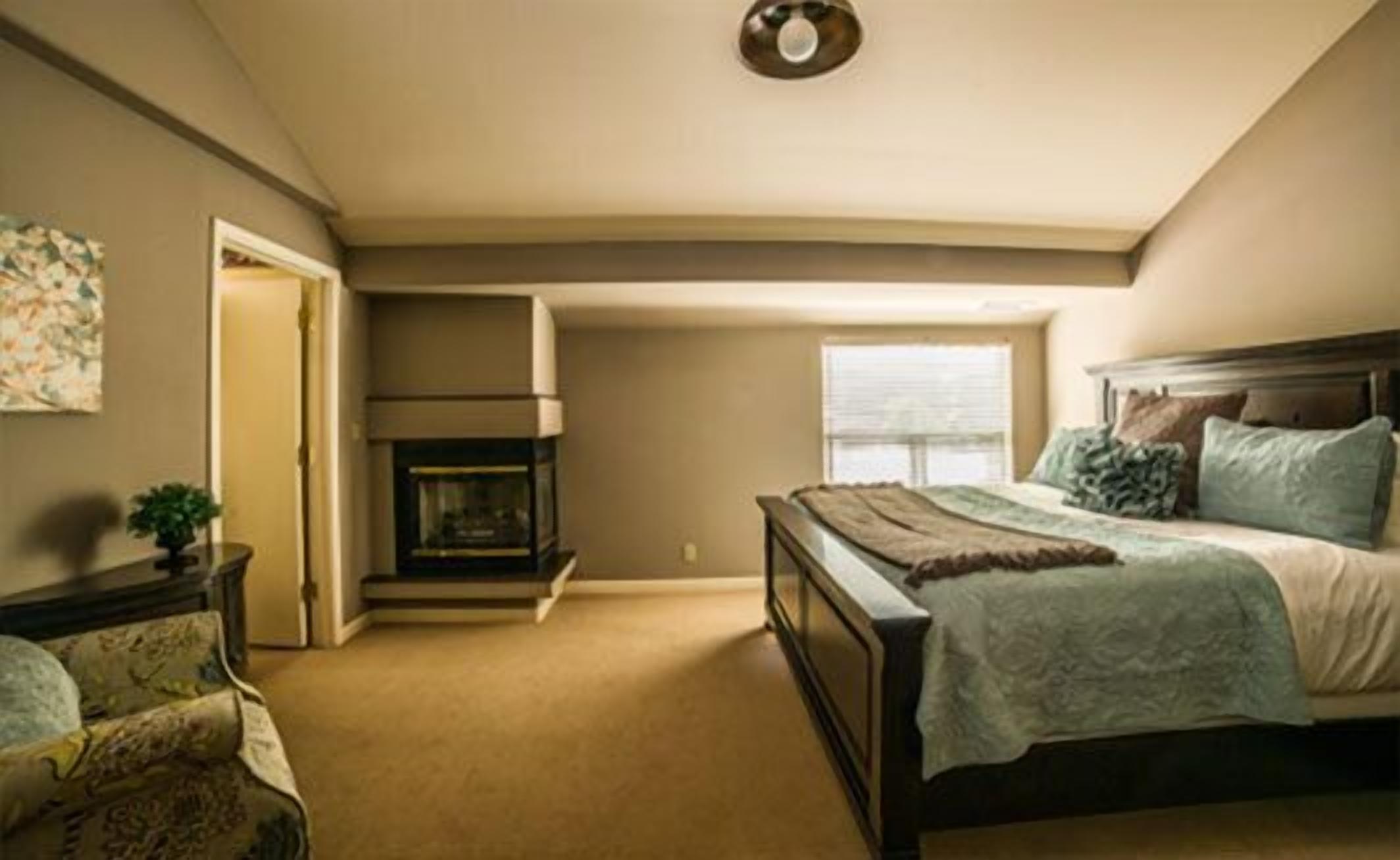 A bedroom with a bed, a fireplace, a window, and a door.