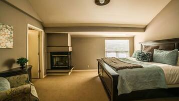 A bedroom with a bed, a fireplace, a window, and a door.