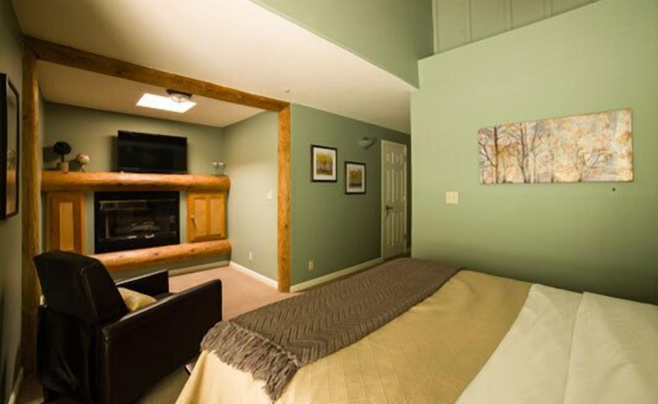 A room with a bed, a chair, a fireplace, and a painting on the wall.