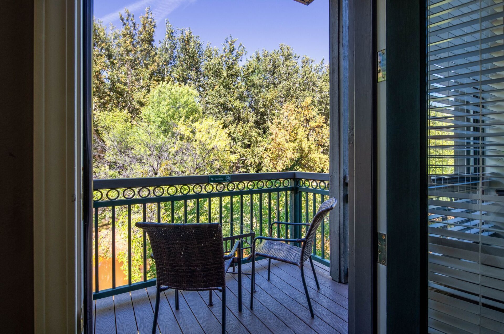 A balcony with wicker chairs and a table, overlooking a forested area.