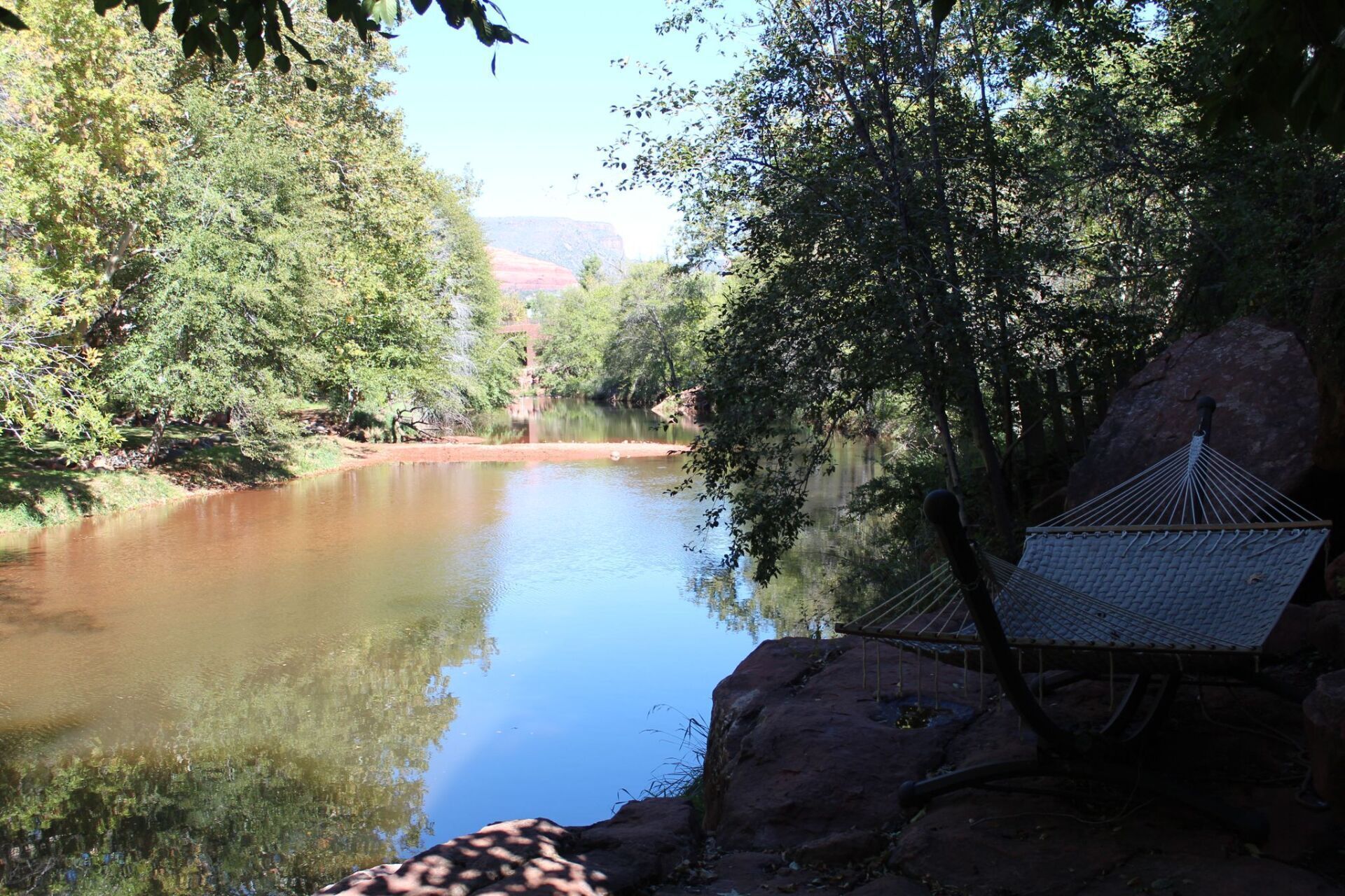 Uma rede sobre uma rocha, próxima a um rio calmo e cercada por árvores.