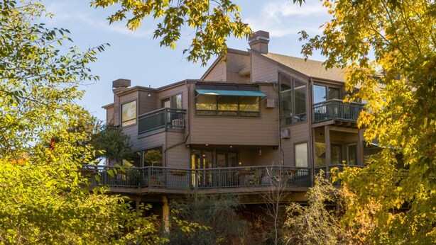 Une maison à plusieurs étages avec un balcon au rez-de-chaussée, entourée d’arbres.
