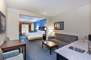 Quarto de hotel com uma cama, um sofá, uma mesa, uma mesinha de centro, uma pia e um quadro na parede.