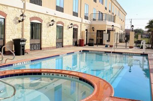 Una piscina con un cartel de prohibición de clavados, un edificio de piedra con varias ventanas y una entrada con portón.