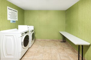 Un lavadero con lavadora y secadora de carga frontal, un banco y un cartel con instrucciones para la ropa.