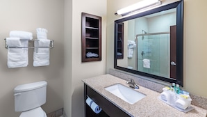 Un bagno con lavandino, specchio, portasciuga, water e uno scaffale con articoli da toilette.