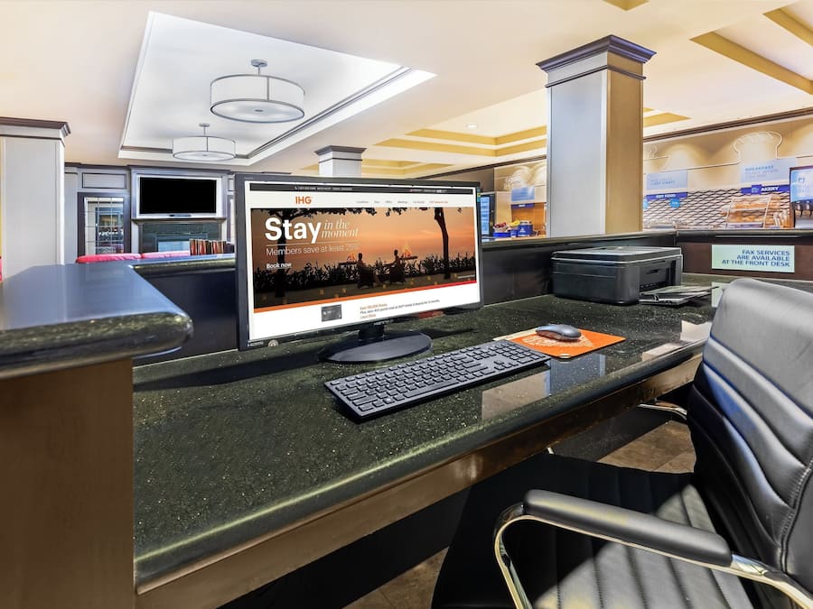 Mostrador de recepción con un monitor de computadora mostrando una pantalla promocional, un teléfono y un fax.