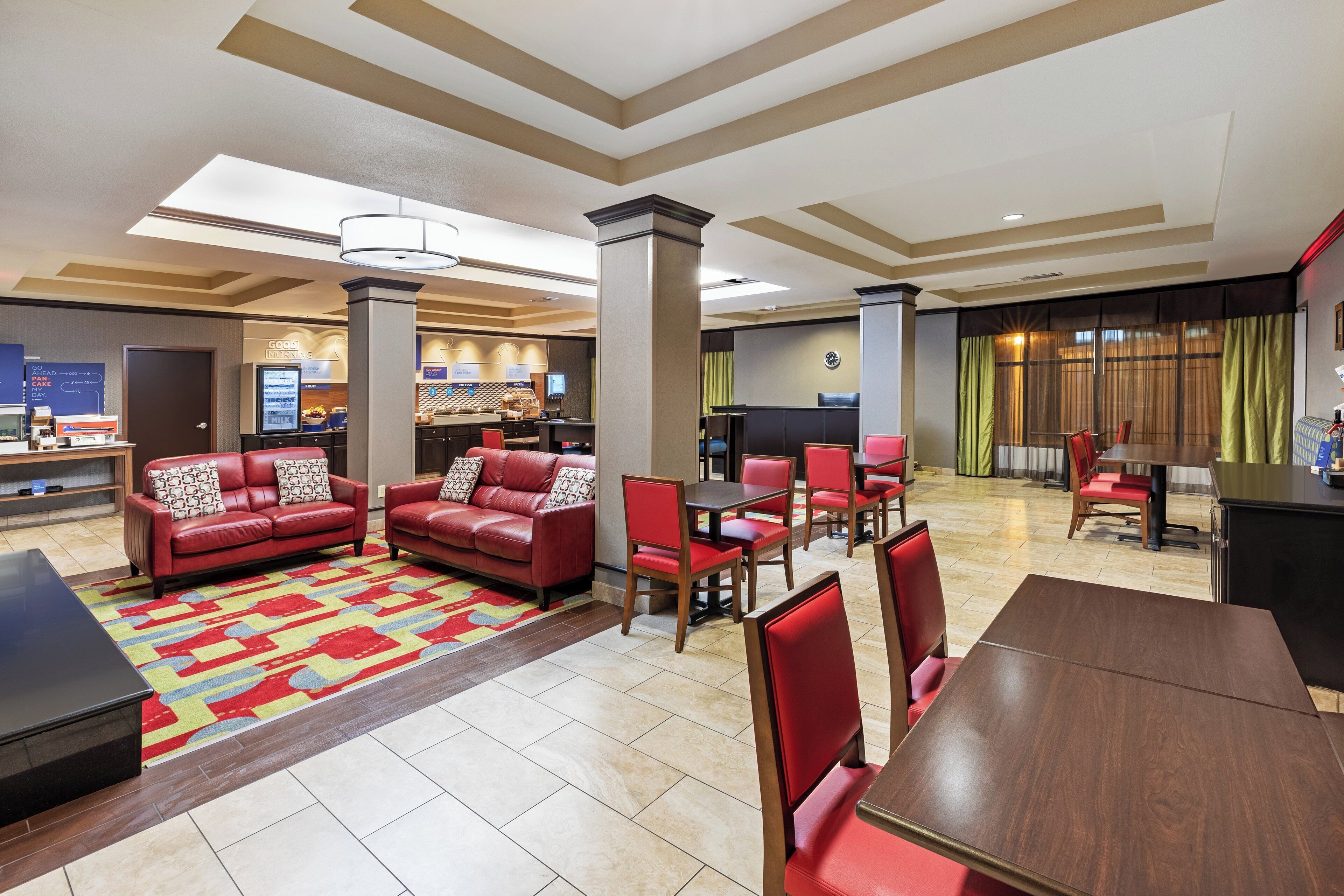 A hotel lobby with a seating area, a breakfast bar, and a dining area.