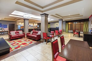 A hotel lobby with a seating area, a breakfast bar, and a dining area.
