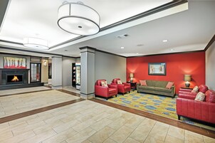 A hotel lobby with a fireplace, red leather sofas, a green sofa, and a patterned carpet.