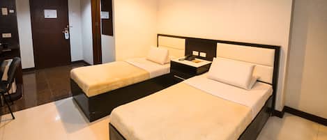A hotel room with two single beds, a desk with a phone, and a chair.