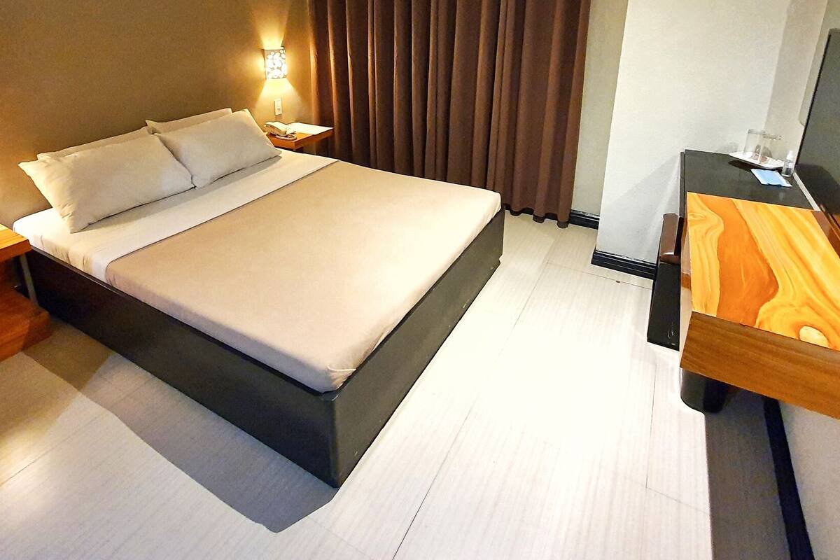 A modern hotel room with a large bed, wooden nightstands, a desk with a chair, and a TV.