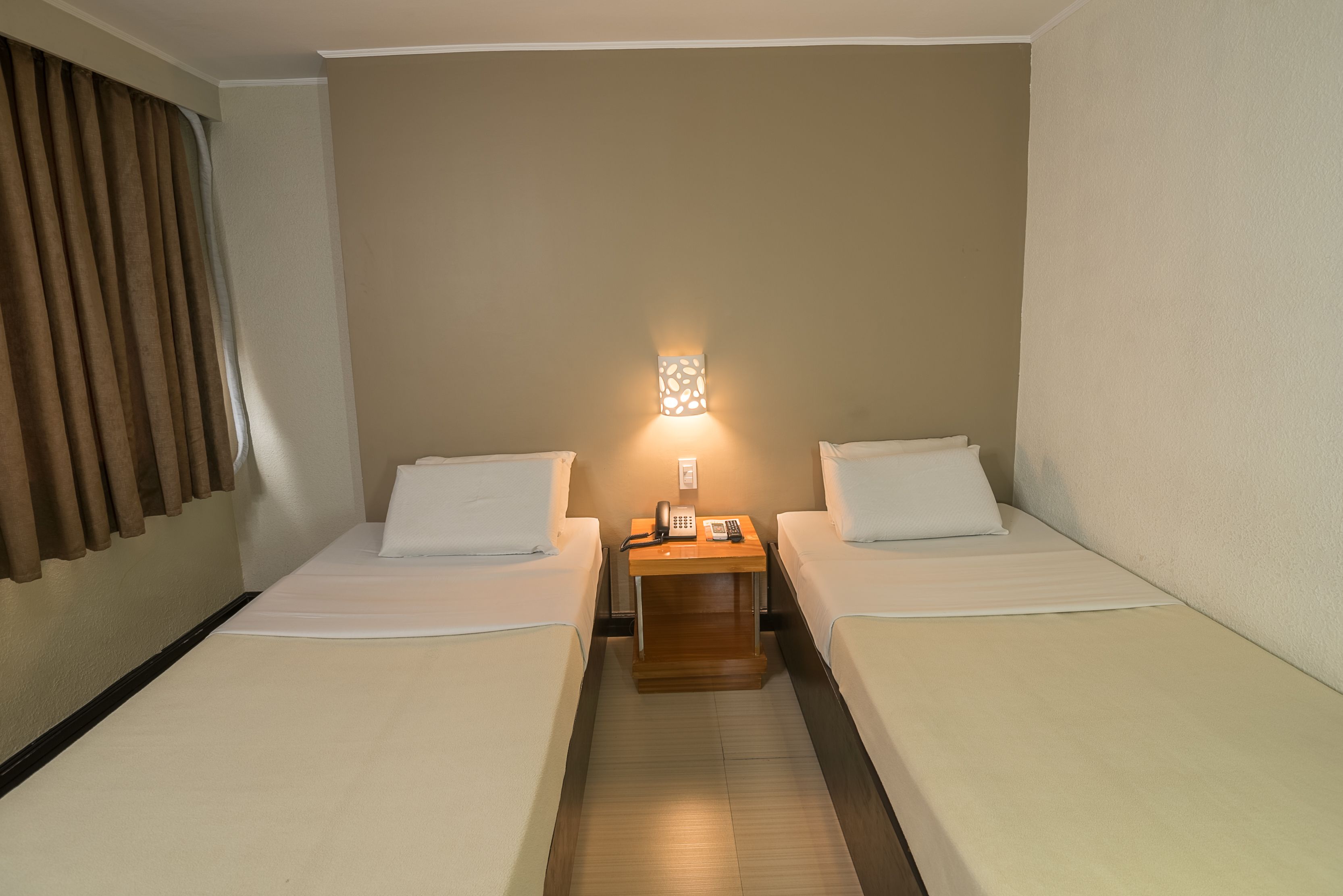 Une chambre d’hôtel avec deux lits simples, une table de chevet avec une lampe et un téléphone.
