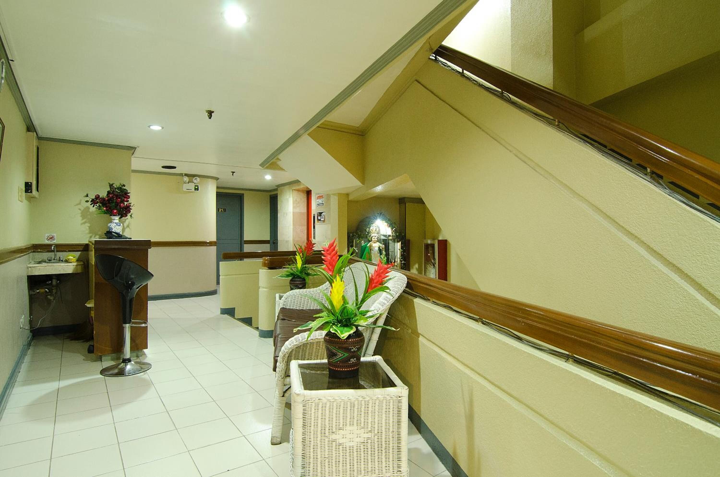 A hotel lobby with a staircase, a reception desk, and a seating area with potted plants.