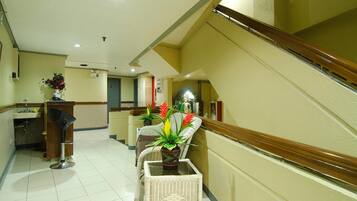 A hotel lobby with a staircase, a reception desk, and a seating area with potted plants.