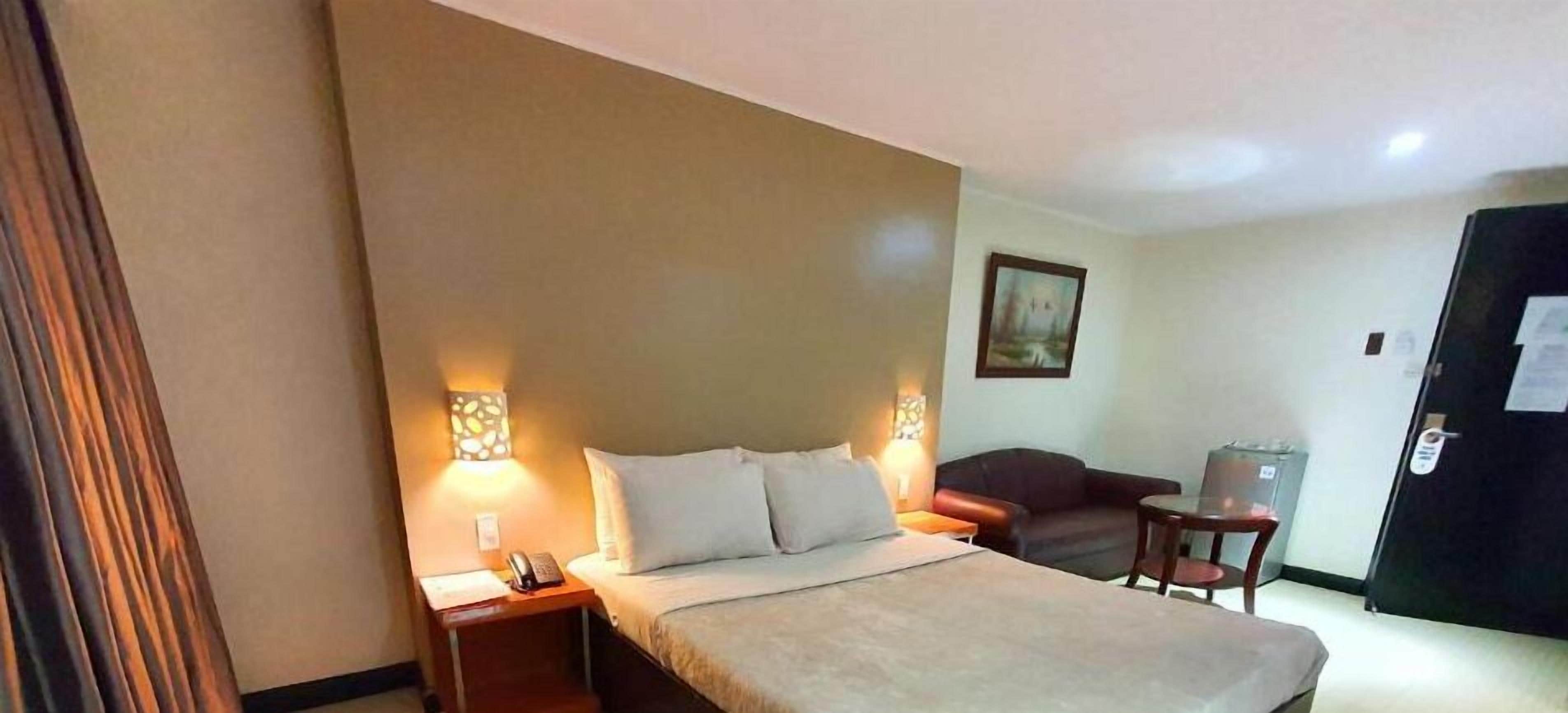 A hotel room with a bed, bedside lamps, a small table, a sofa, and a door.