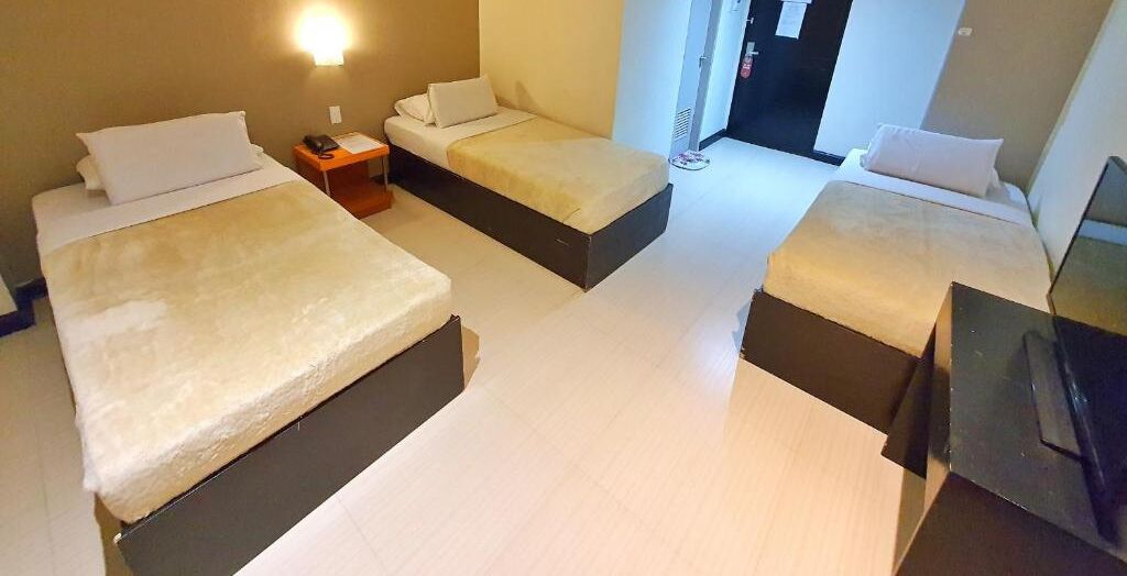 Habitación de hotel con tres camas, una mesita de noche con teléfono y un televisor sobre un mueble.