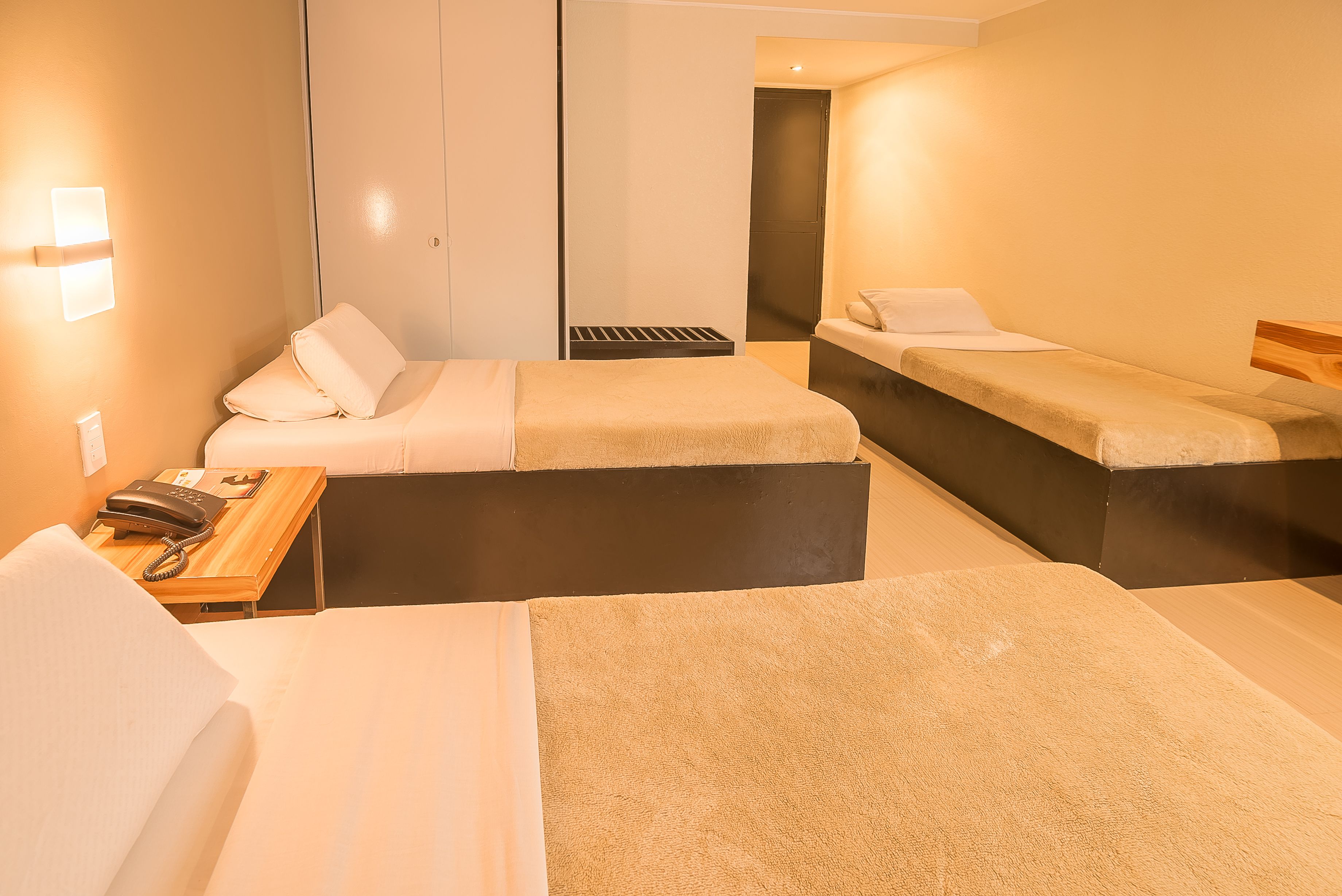 A hotel room with two beds, a desk with a telephone, and a wall-mounted light.