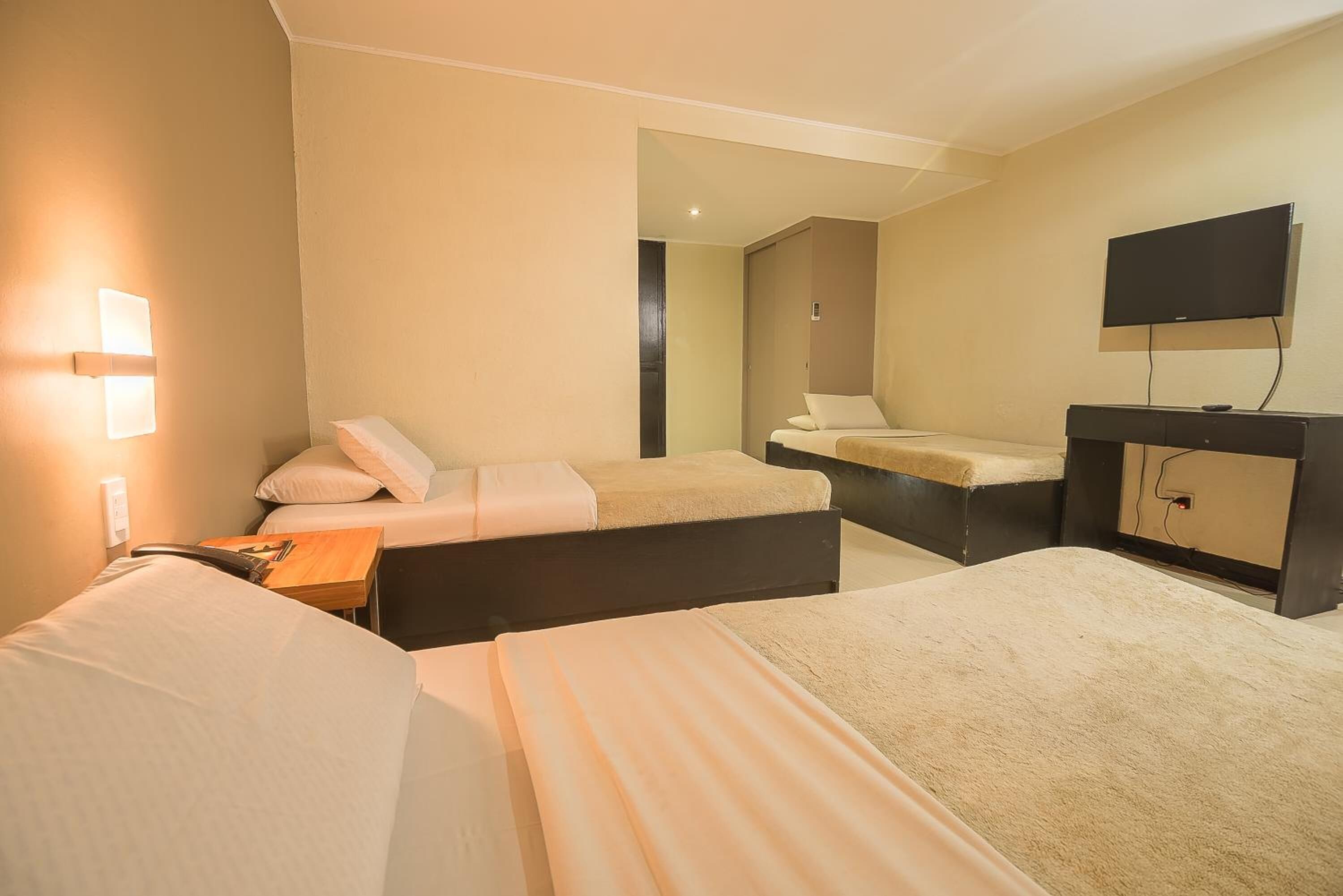A hotel room with two beds, a desk, a TV, and a mirror.