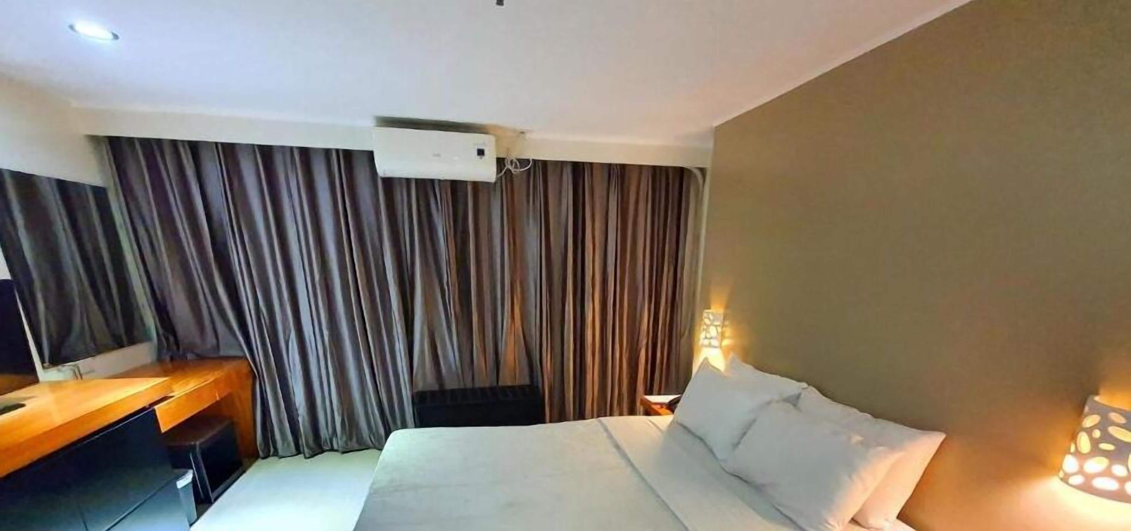A hotel room with a bed, a desk, and curtains.